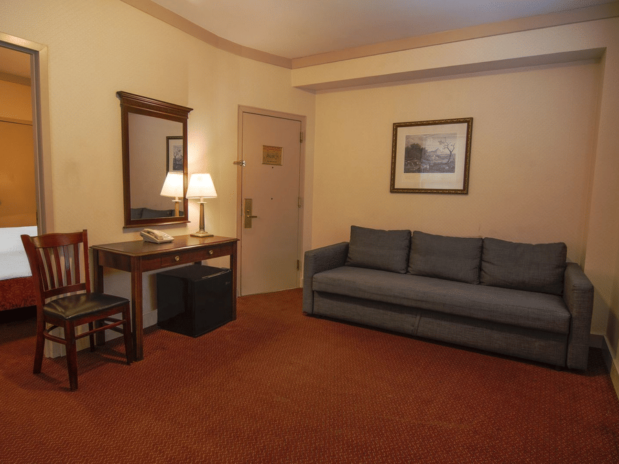 Spacious room at Night Hotel Broadway featuring a sofa, work desk, chair, lamp, and warm ambient lighting.