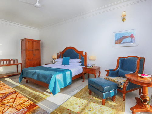 Spacious deluxe room featuring double bed, wooden furniture, work desk, and warm lighting at Fateh Niwas, Udaipur.