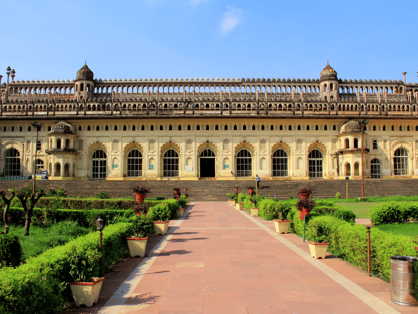 A wide-angle view of a large, beautiful historical palace with a long, stone walkway leading up to it through a green lawn.