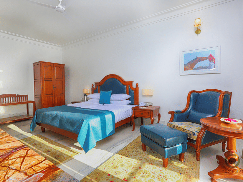 Spacious deluxe room featuring double bed, wooden furniture, work desk, and warm lighting at Fateh Niwas, Udaipur.