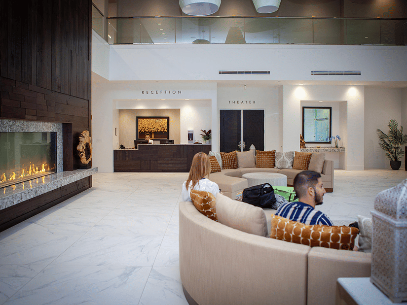The lobby of YO1 Longevity and Health Resorts with guests seated on a curved sofa near a sleek fireplace, creating a warm and welcoming first impression