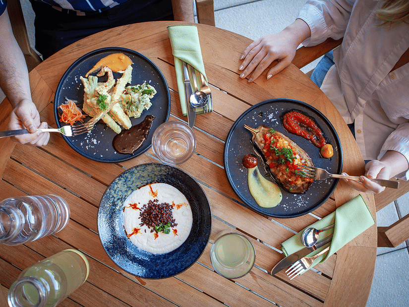 A round dining table with three platters of food on it and a couple of people eating at YO1