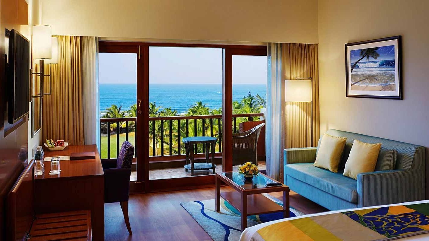 A cozy hotel room with a balcony offering stunning ocean views, featuring comfortable seating and elegant decor.