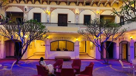 A facade image of Roop Vilas Palace illuminated and people sitting in comfortable chairs in an open area