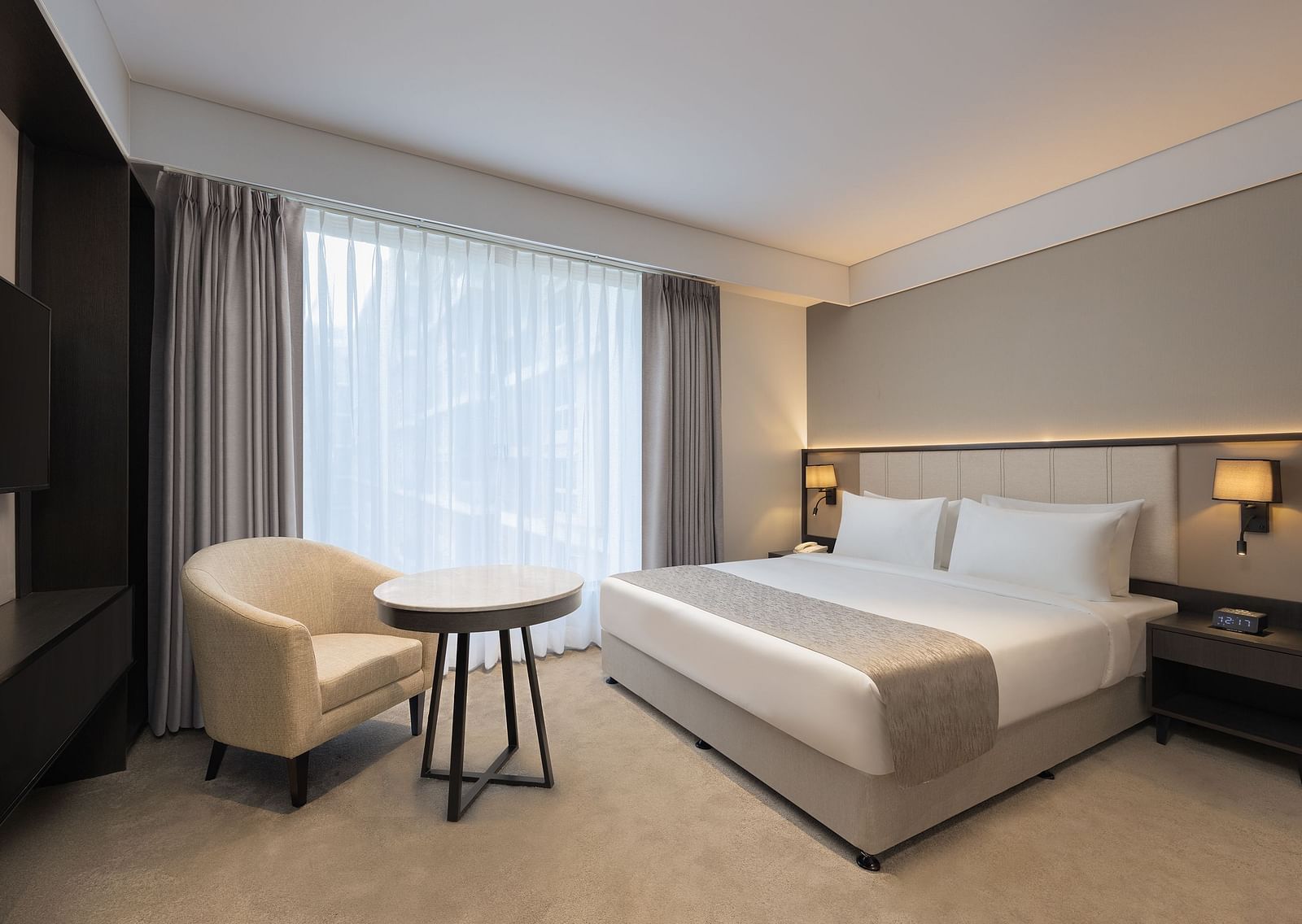 Deluxe King Room with a king size bed and a comfortable chair beside a large window at Essentia Premiere, Pune. 