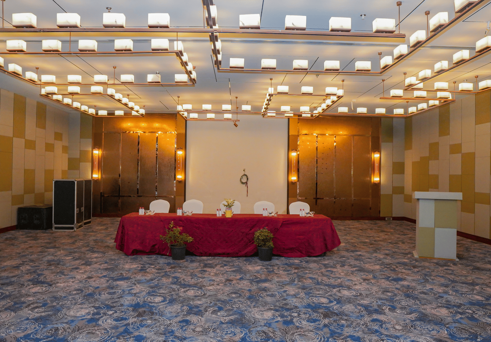 A photo of a stage area in an event room, with a table draped in a red cloth and a podium, waiting for a speaker.