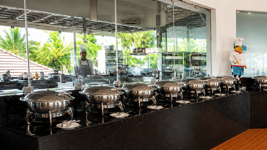 Restaurant buffet counter with chafing dishes and scenic garden views at Chariot Beach Resort, offering a fresh and inviting dining experience.
