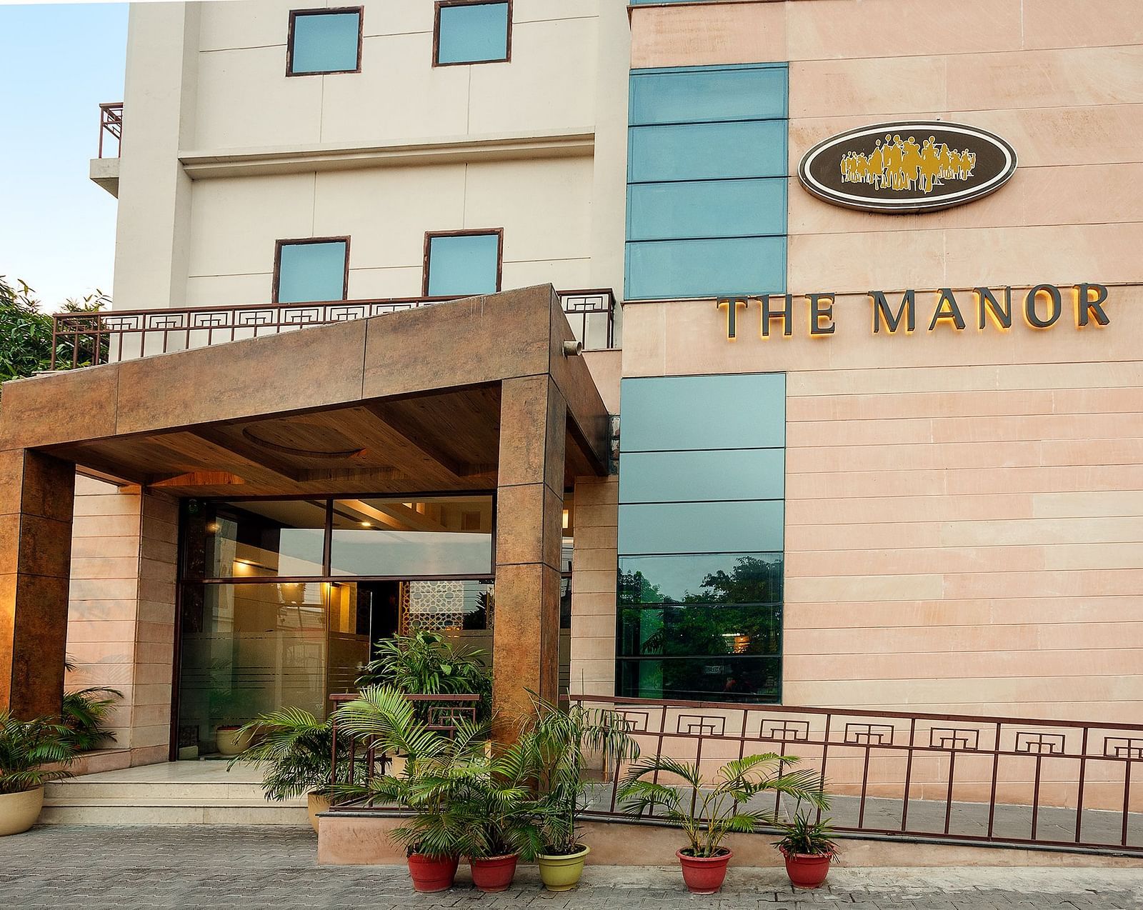 facade image of The Manor hotel, showcasing a modern entrance with potted plants and a clear blue sky above - The Manor, Bareilly