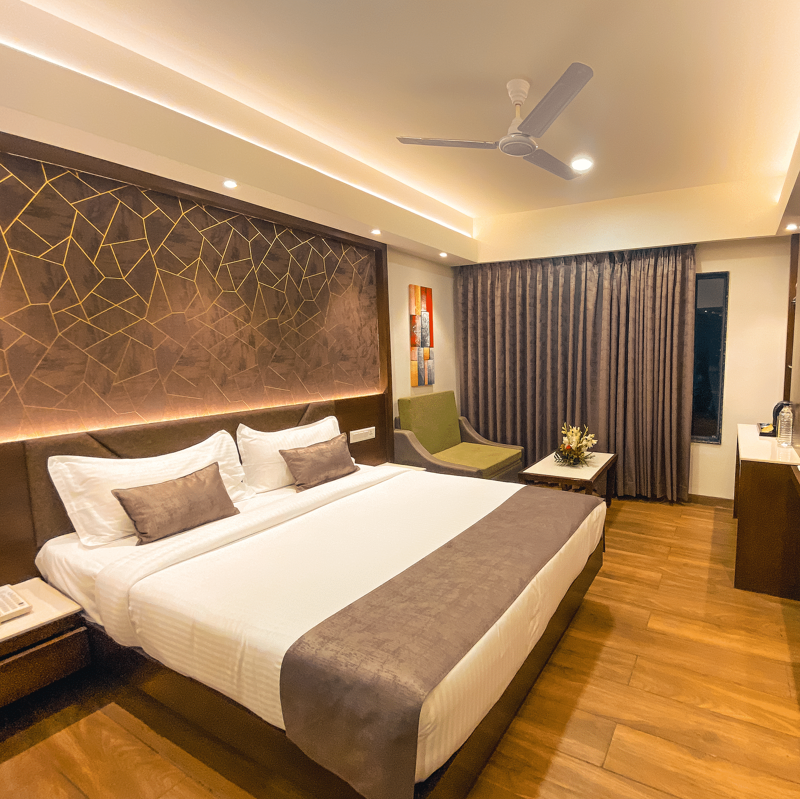 a bedroom with a large bed facing a mounted television and a green chair in the corner - Jardin Hotels, Indore
