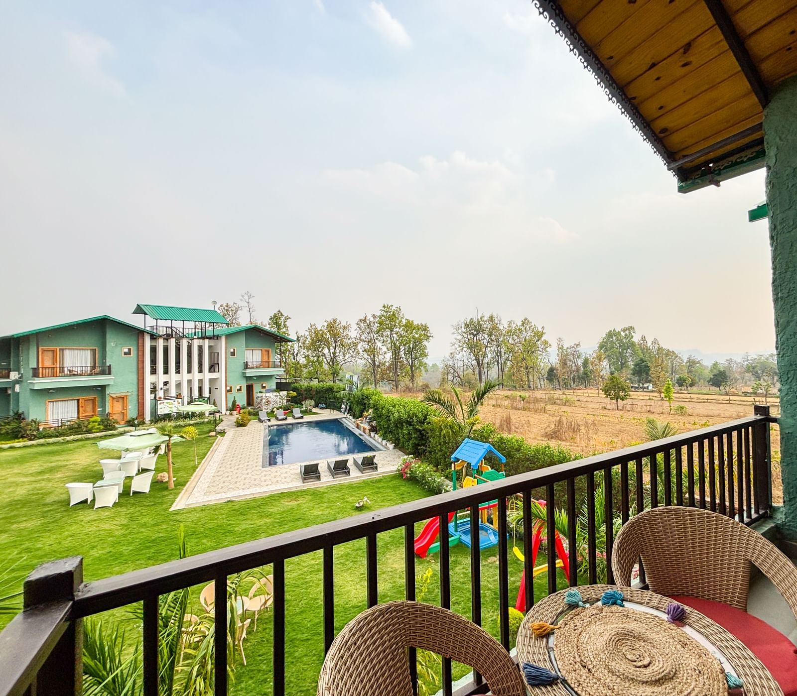 A wide angle shot of a balcony overlooking a bright lawn area under a clear blue sky in the background at Corbett Nirvana Resort.