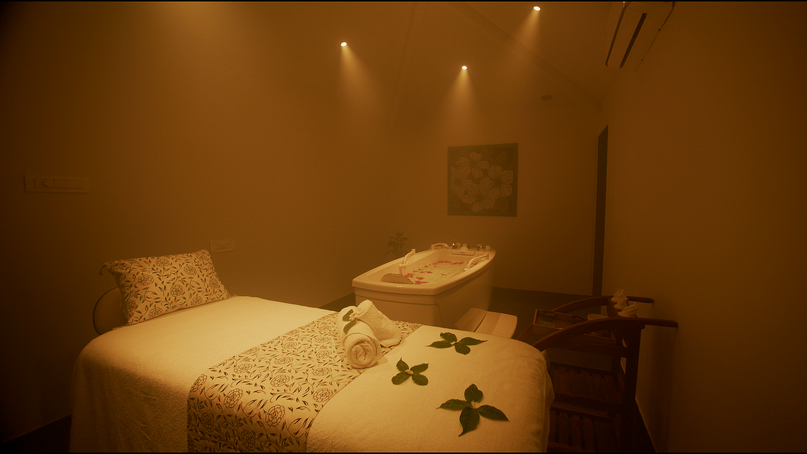 A dimly lit spa room with a massage table and bathtub - Gamyam Retreat