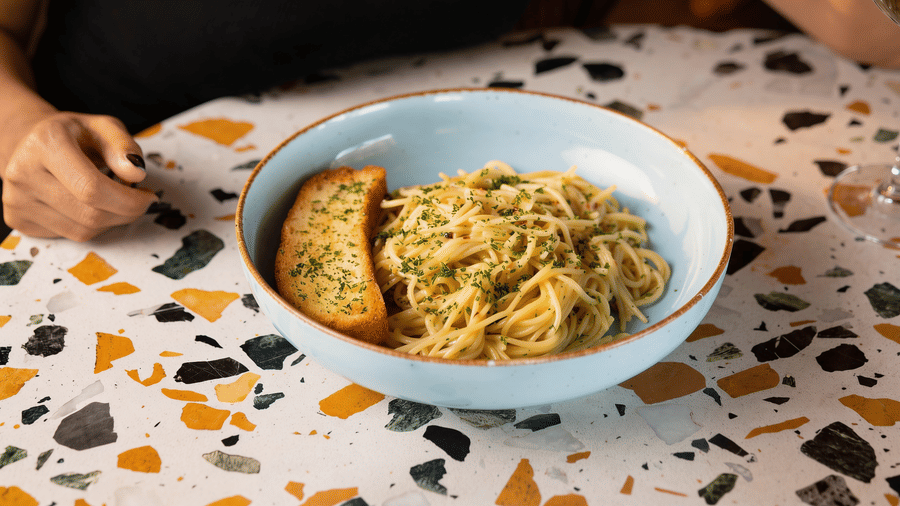 A bowl filled with creamy pasta and a piece of garlic bread is served on a terrazzo patterned dining table at the property, The Sierra - By The Lake.