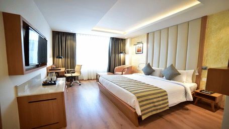 Spacious hotel bedroom featuring a king bed with an upholstered headboard, wood flooring, and a window seating area.