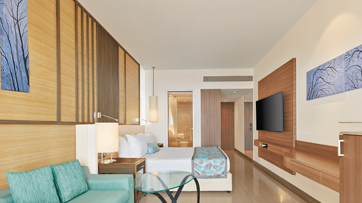 Stylish modern room with wooden accents, pastel furnishings, a wall-mounted TV and an open layout leading to a spacious ensuite – The Resort, Mumbai