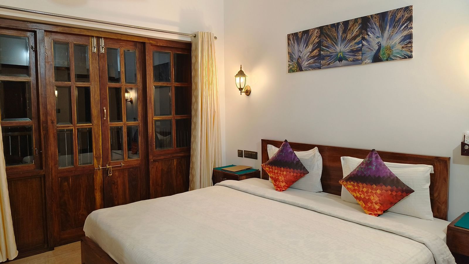 A double bed with colourful pillows and a frame hanging on the wall at 103 room at Ananda Holiday Home, Wayanad 4