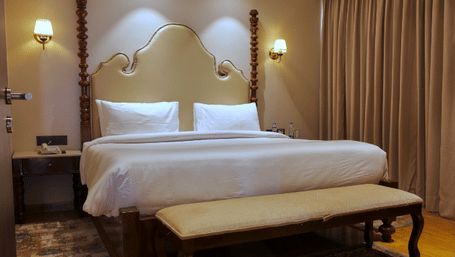 Royal Suite at Raj Leela Heritage Resort by Estherea, Ranakpur featuring a king size bed, wooden bench, bedside tables, wall lamps, and curtains.  