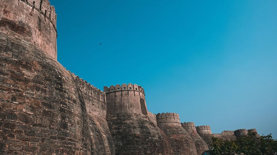 Old tall wall with round like curves perching on the outside, the wall has black  impressions on it under a blue sky 