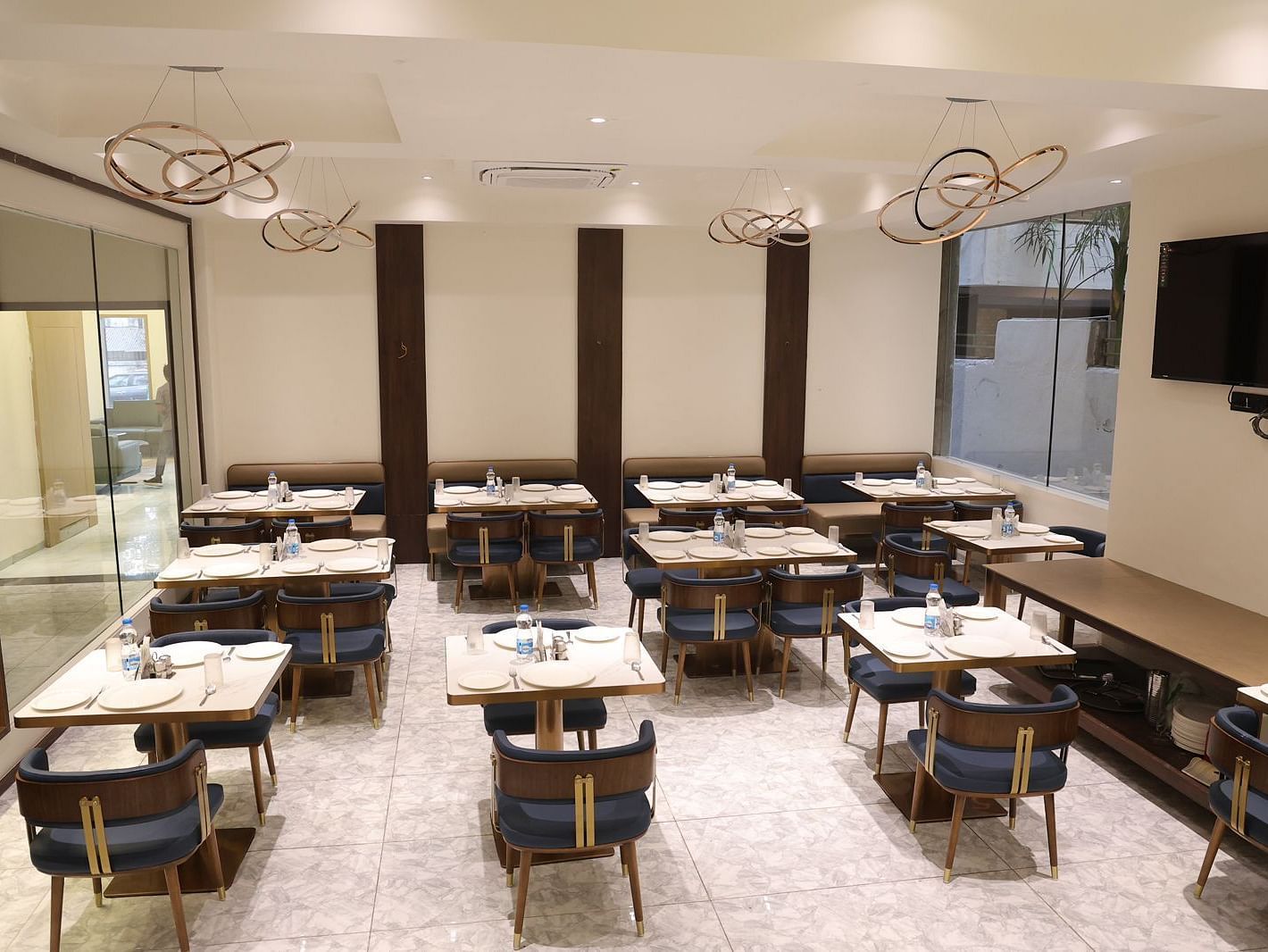 A brightly lit dining area at Lords Eco inn Jamnagar Maheshwari Nagar with multiple tables chairs and stylish lighting.