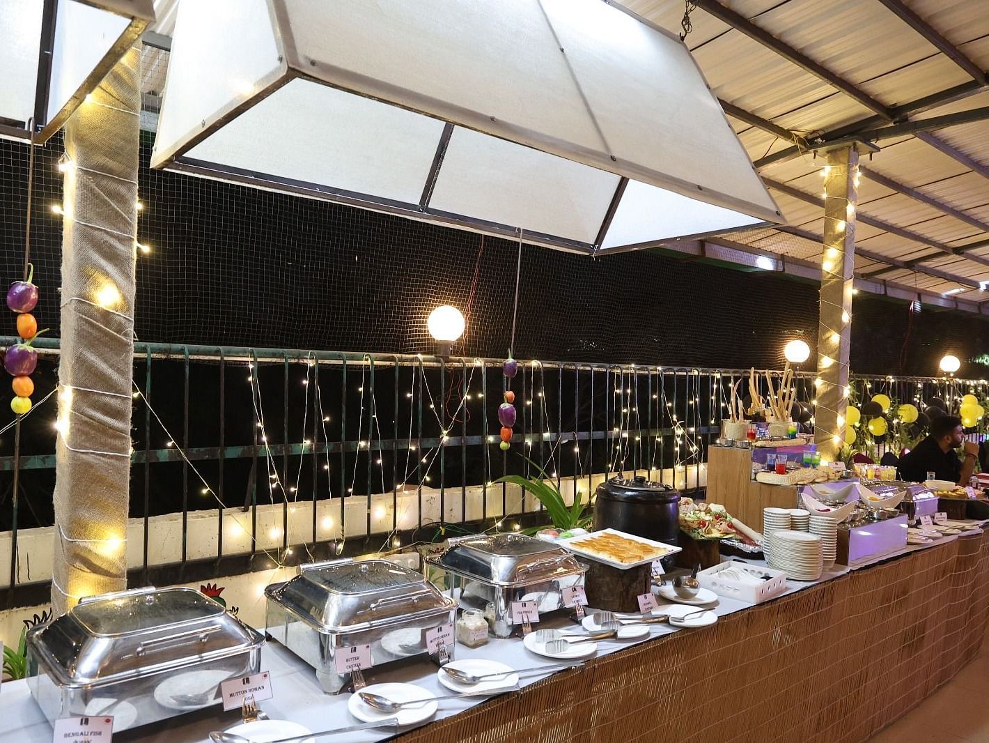 An outdoor dining area at night features buffet stations under illuminated canopies - Lords Inn Vadodara