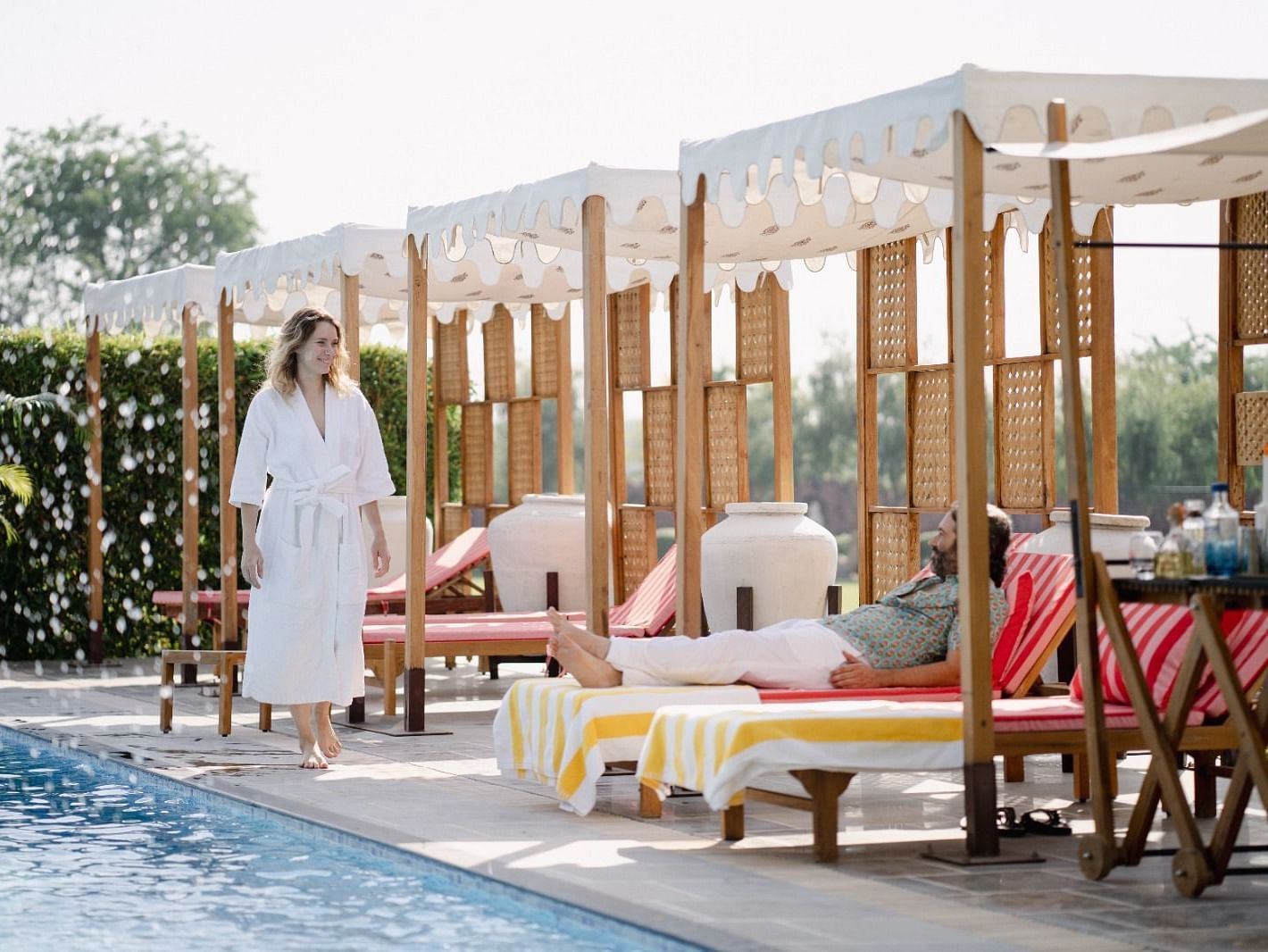 A man seating beside a swimming pool and a woman walking beside it at Surpura Bagh.