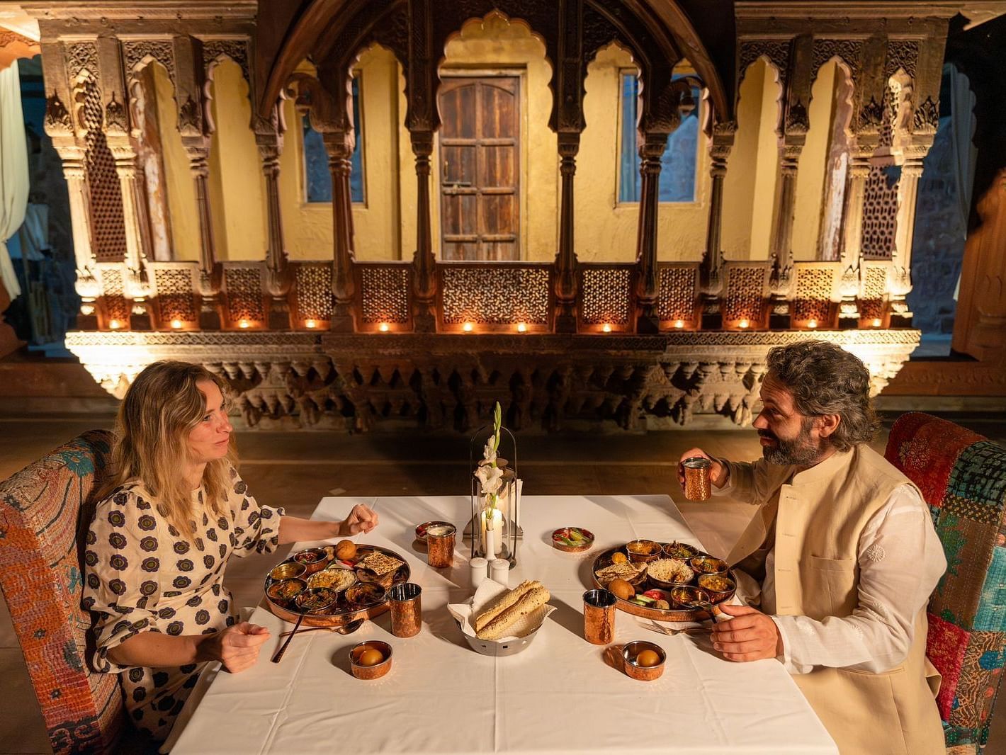 A man and woman in a dining area with an assortment of food placed on the table at Aerial view of a swimming pool with lounge chairs on the side at Surpura Bagh.