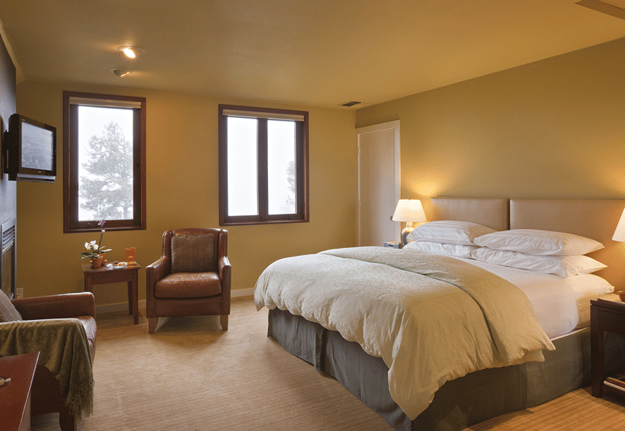 A large hotel room with a king-size bed, leather armchair, and wooden nightstand.