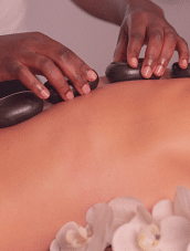A person on a massage table with white flowers in the surrounding, receiving a hot stone massage.