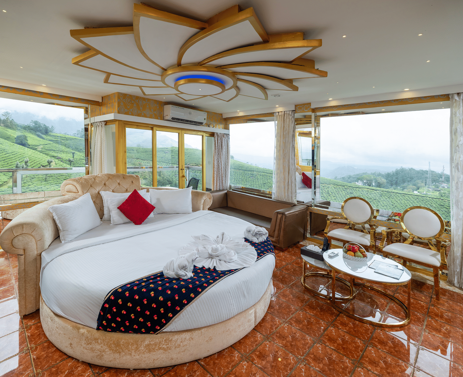 An interior view of the Jacuzzi 180-degree Suite at Parakkat Nature Hotel and Resorts, Munnar, featuring a large round bed, plush decorative pillows, and elaborate gold-toned ceiling accents.
