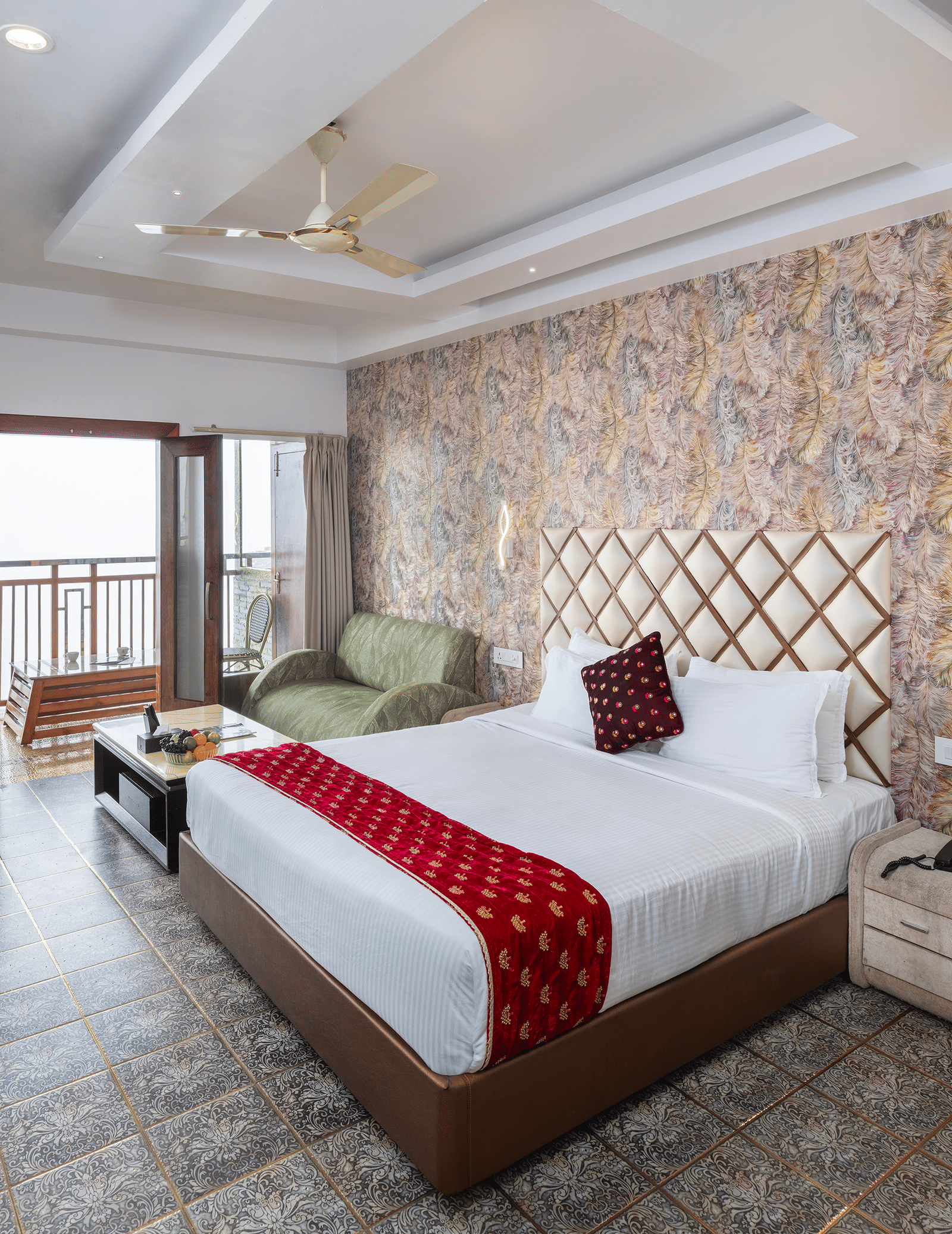 The interior of the Premium Club Suite at Parakkat Nature Hotel and Resorts, Munnar, featuring a large bed, a stone-patterned accent wall, a seating area, and sliding doors to the balcony.