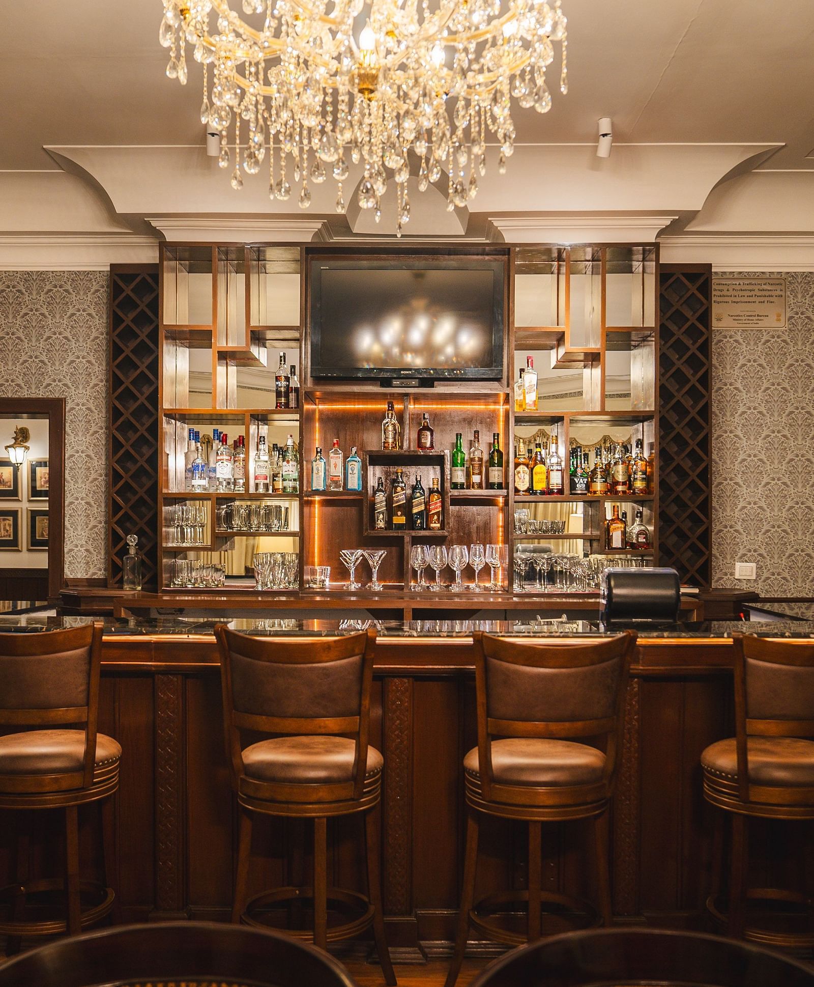 A well-designed bar with high stools and a wide selection of spirits, featuring an elegant chandelier and inviting wooden décor.