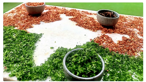 Different types of condiments, leaves, cardamom, and chilly flakes placed on a mat. The condiments are spread outside of the outline of Indian map.