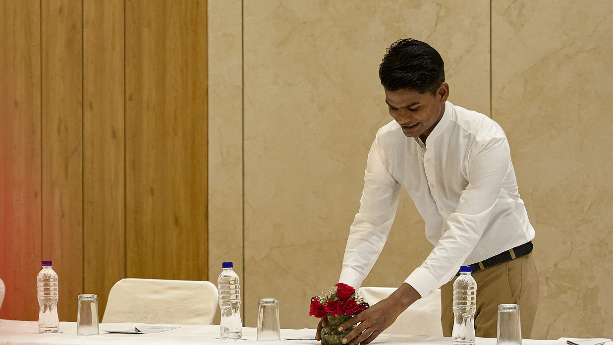 A man setting floral arrangements on a long white table featuring bottles of water placed neatly on it.