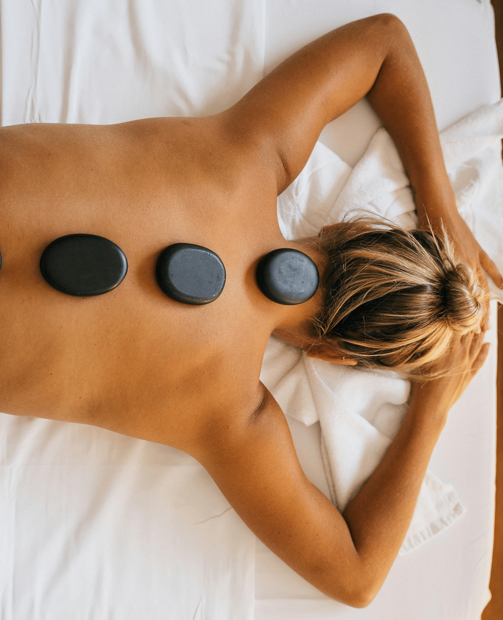 A woman lying down with back with black stones kept over her spine