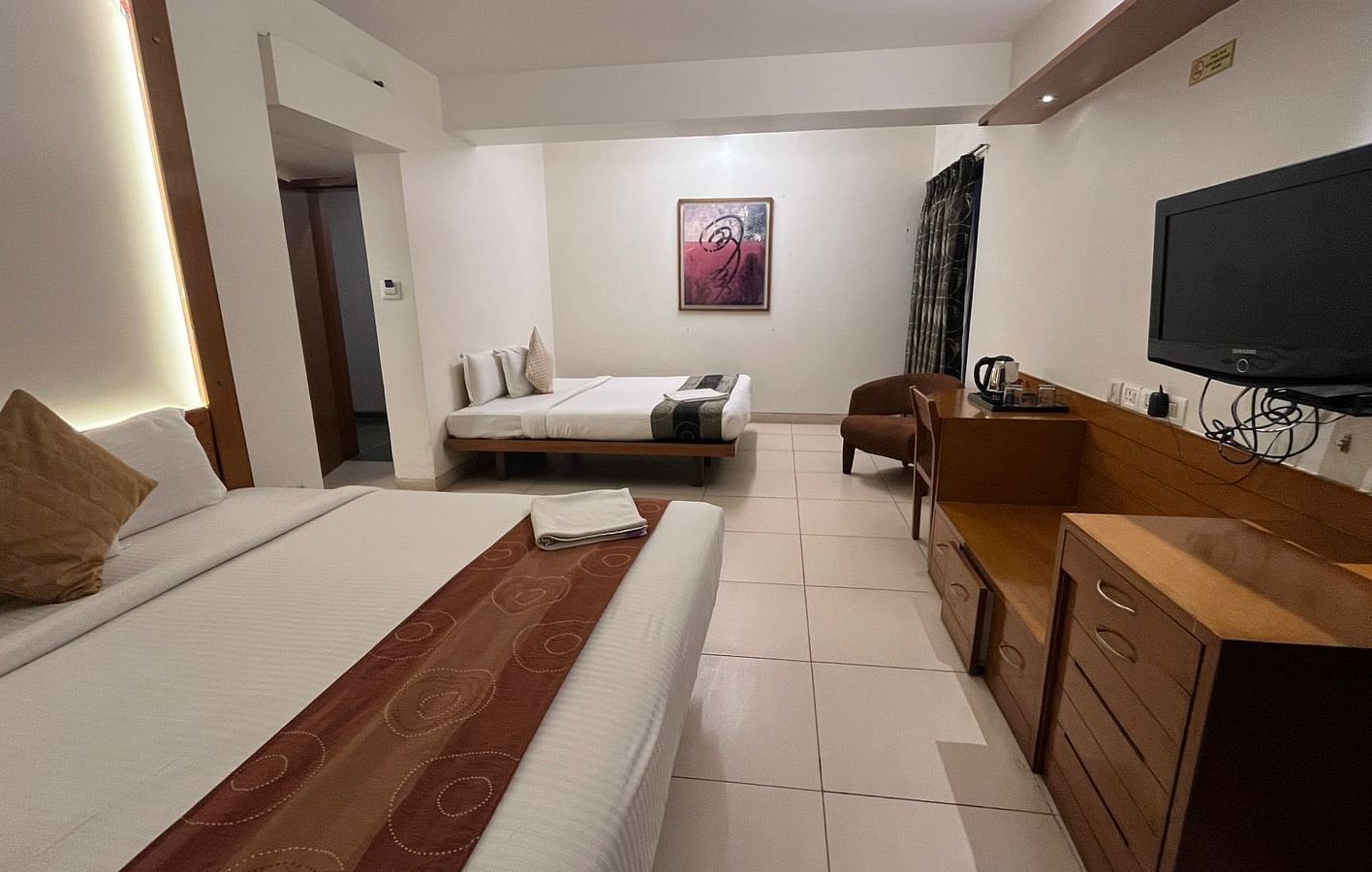 Hotel room featuring two beds with coordinated runners, a wall-mounted television, a functional wooden desk and chair, and a framed artwork - Astra Hotels & Suites, Spice Garden Layout