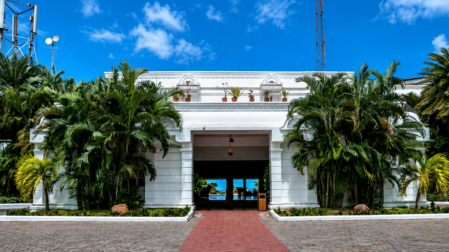 Front view of Chariot Beach Resort showcasing its elegant white façade, palm trees, and a welcoming red pathway entrance to the resort.