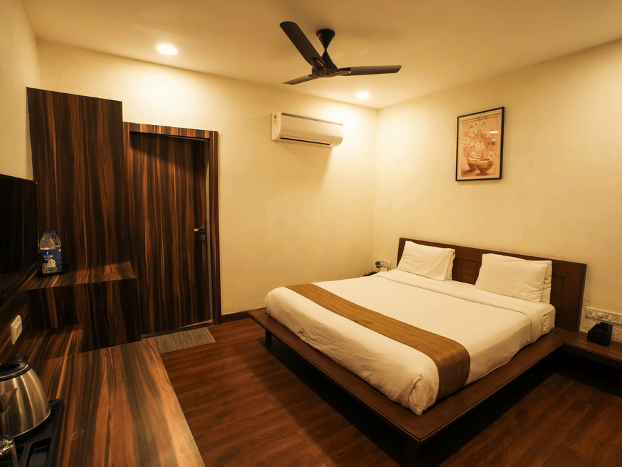 A spacious bedroom at Adamo The Village showcasing a neatly made bed, wooden flooring, and minimal decor.