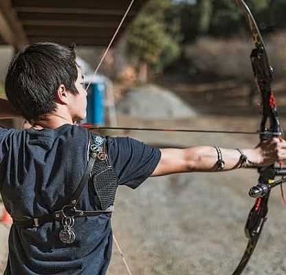 Back shot of a person with a bow and arrow aiming towards the target.