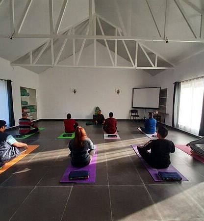a group of people practicing yoga inside a room - Neer Ganga Resorts