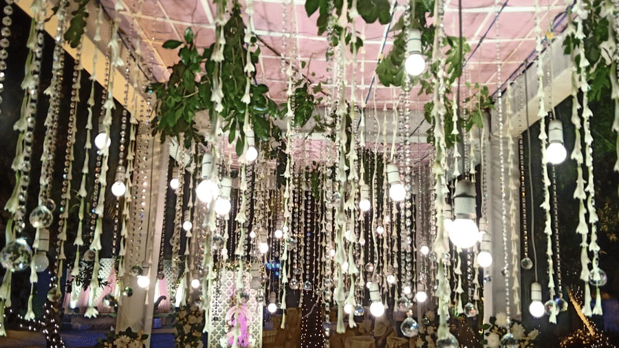 A beautifully decorated event ceiling at Vedic Village Spa Resort featuring hanging floral arrangements green foliage crystal strings and warm pendant lights creating an enchanting indoor ambiance.