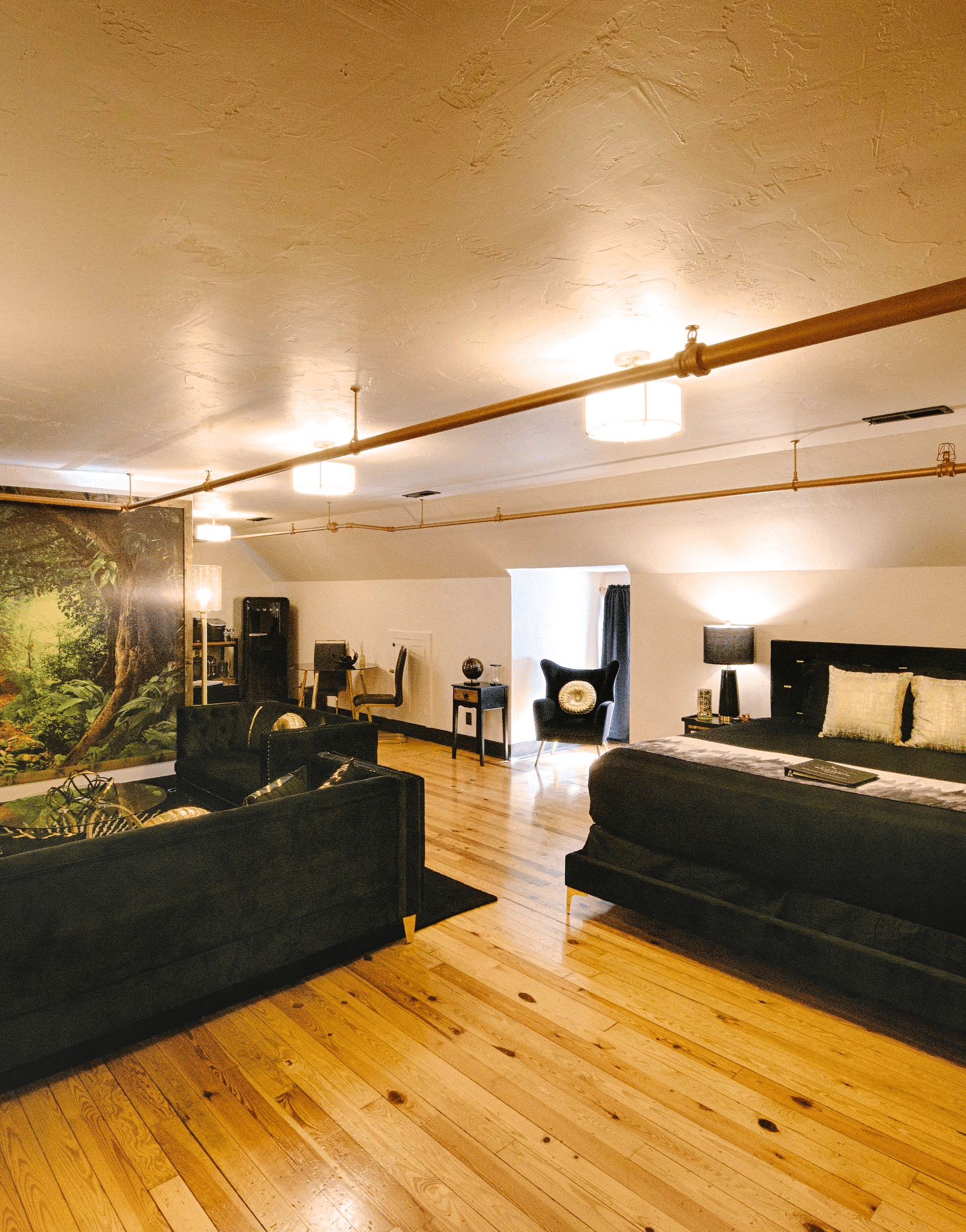 a spacious bedroom with a cozy double bed and black couch set in the common seating area with a jungle mastiff made in the feature wall of the suite - Historic Tapoco Lodge