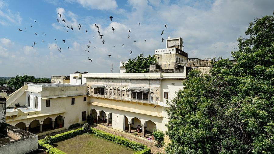 A bird's-eye view of Fort Barli reveals its courtyard, white buildings, and surrounding landscape under a partly cloudy sky.