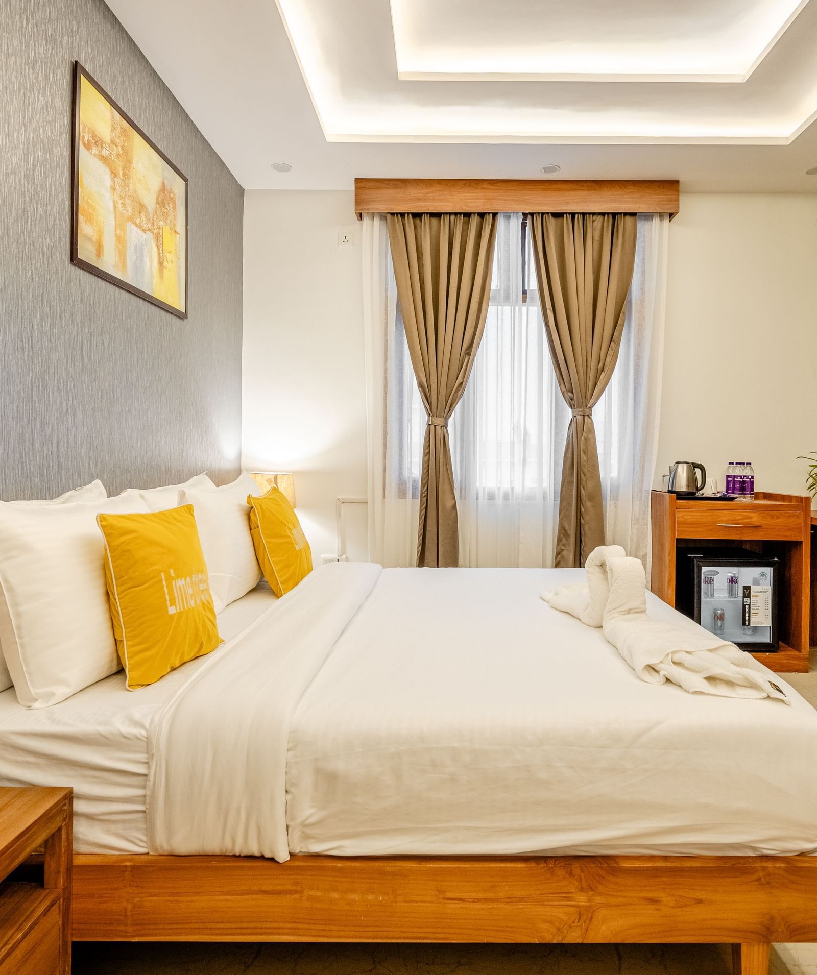 A bedroom with a king bed, pillows, cushions, kettle, water bottles, minibar, and wall decor at Lime Tree Hotels & Service Apartment Pvt Ltd.