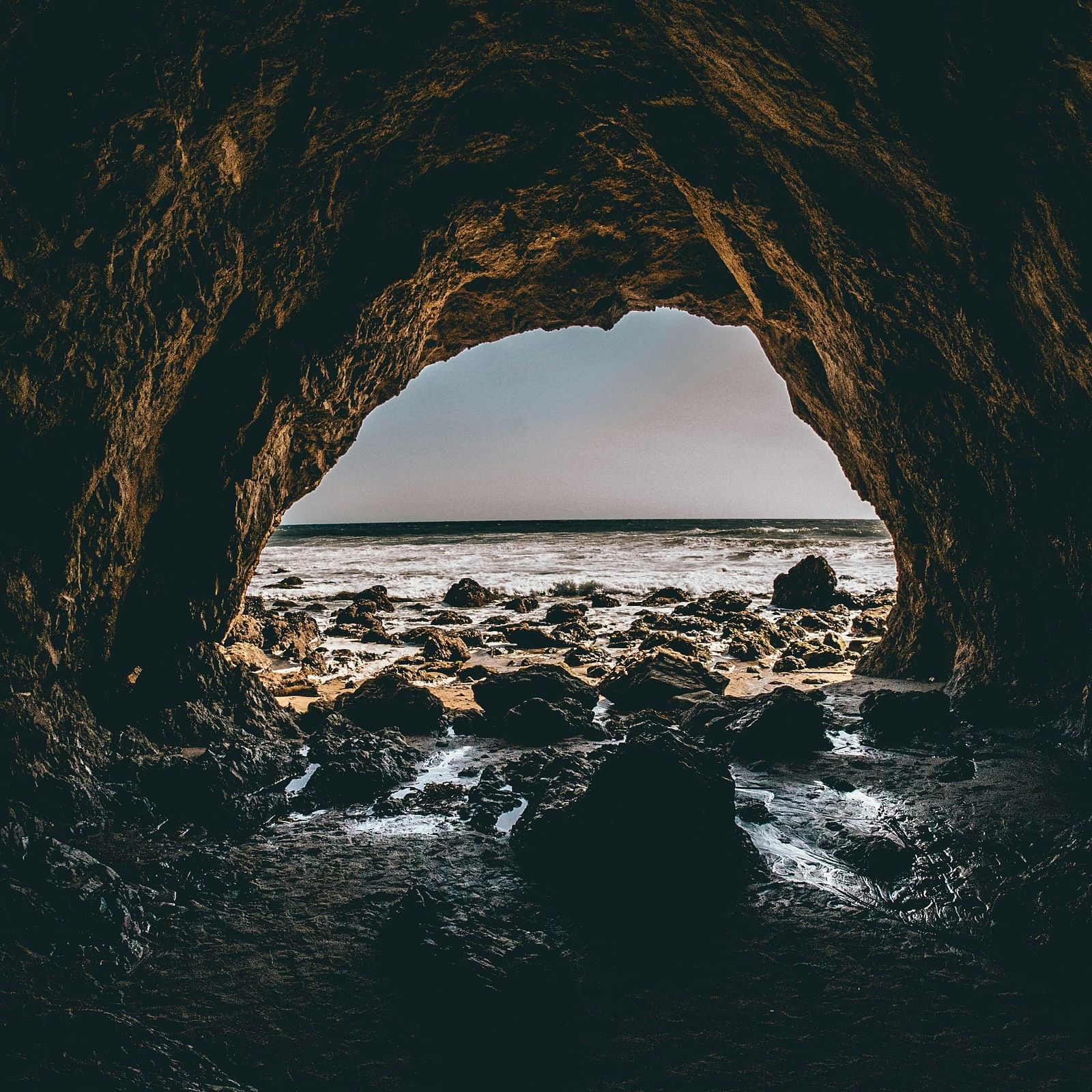 A view from inside a dark cave looking out towards a rocky beach and the ocean.