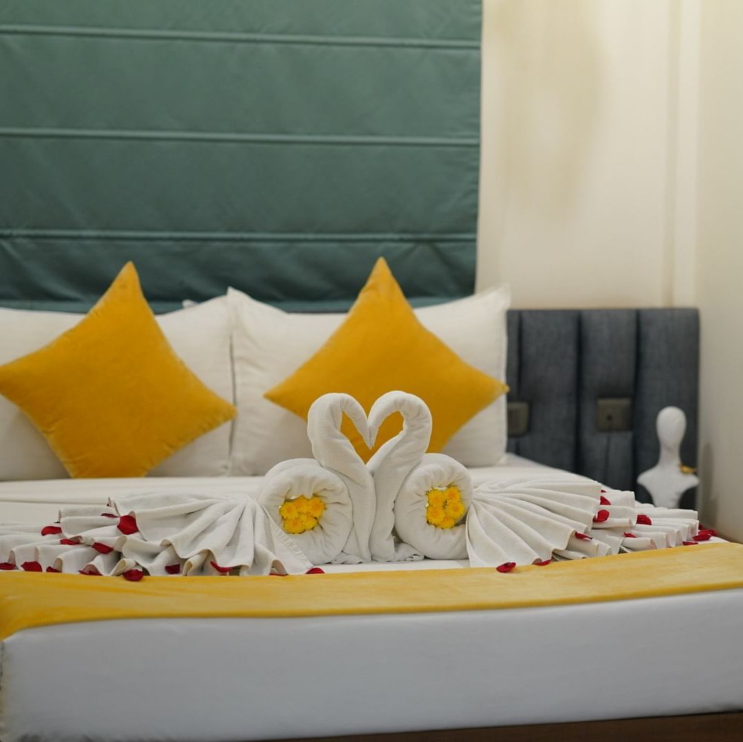 A room with a neatly made double bed adorned with yellow and towels shaped into swans, scattered with rose petals for a welcoming touch at Hotel Kyzen Smartstays – Smart, Reliable, Kyzen