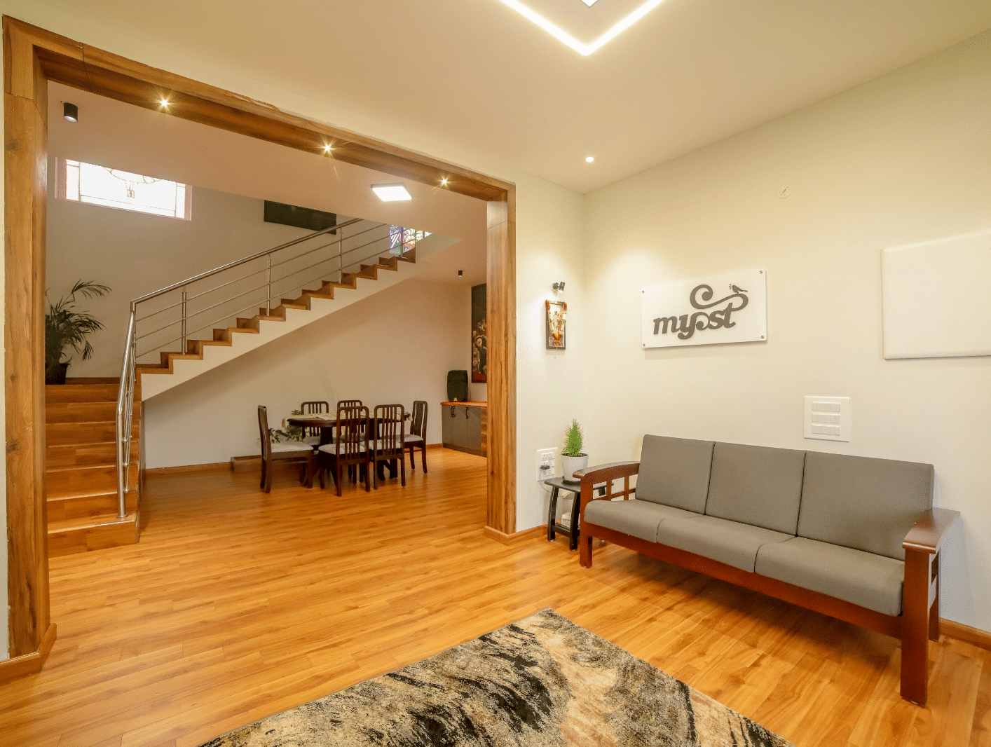 An upholstered multi-seater sofa seen in the living area of MYST Resorts, Doddabetta, Ooty, seen on wooden flooring, and the dining table seen in another section of the villa.