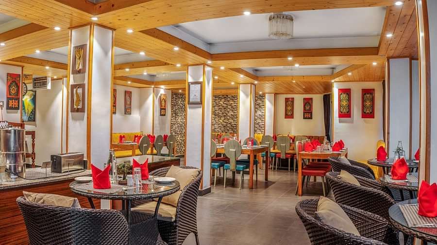 Modern restaurant interior with neatly arranged tables and chairs, red napkins on tables, warm lighting, and decorative wall art at Summit Swiss Heritage Resort & Spa, Mall Road