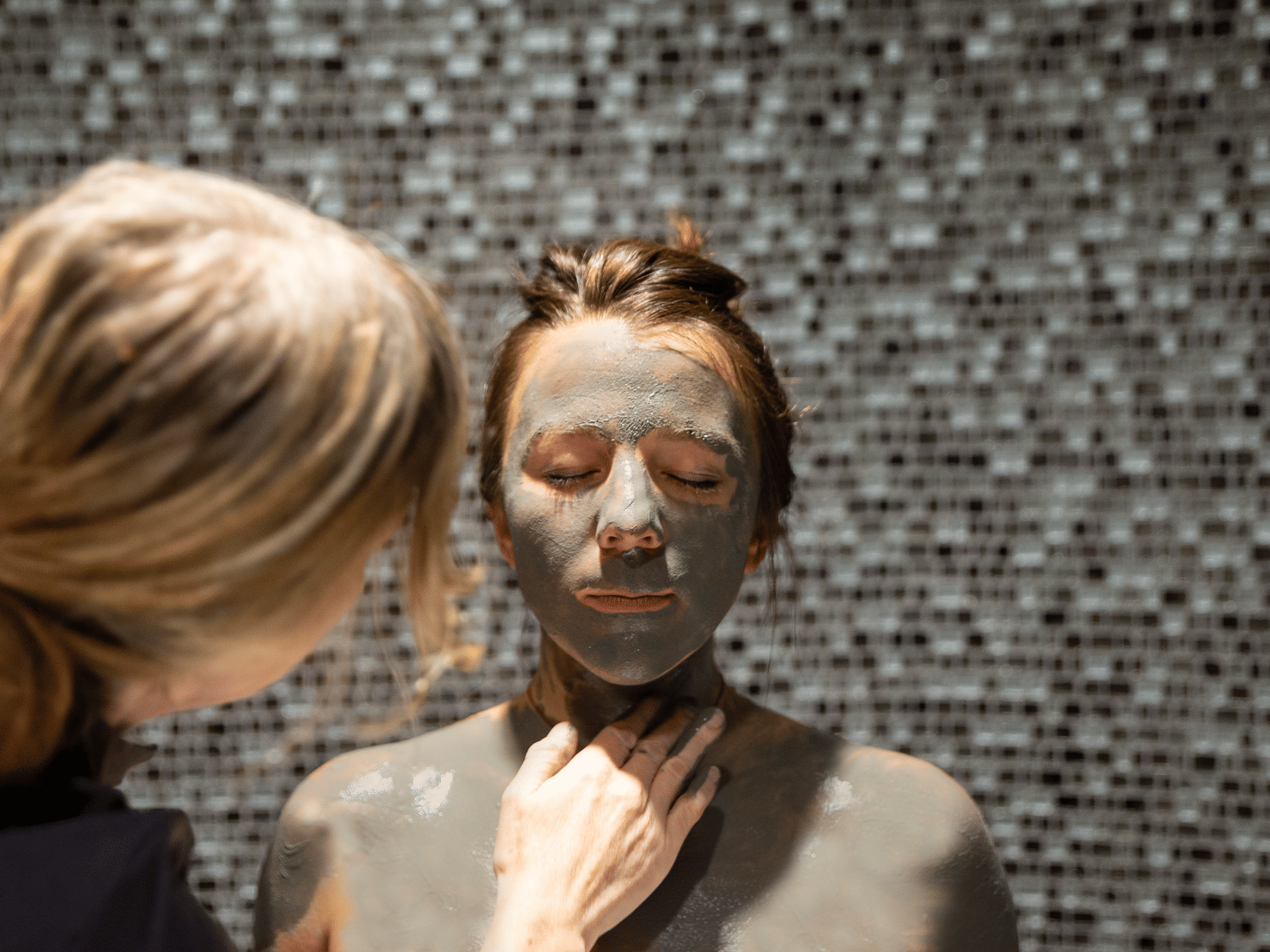 A therapist at YO1 Longevity Health Resorts Catskills applying mud to the face and body of a woman sitting with her eyes closed