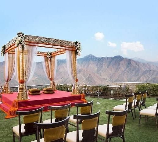 a mandap set up meant for wedding ceremony on manicured lawn with chairs facing it and in the background there are hils at a distance- neer ganga Resorts