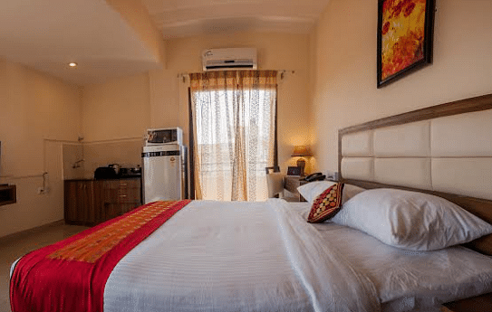 A hotel room with a neatly made bed, television, and partially visible window | Astra Hotels and Suites Electronic City