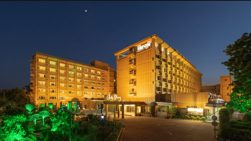 Facade of Clarks Shiraz, Agra, with multiple floors, captured during the night, with lights highlighting focus towards the leaves nearby.